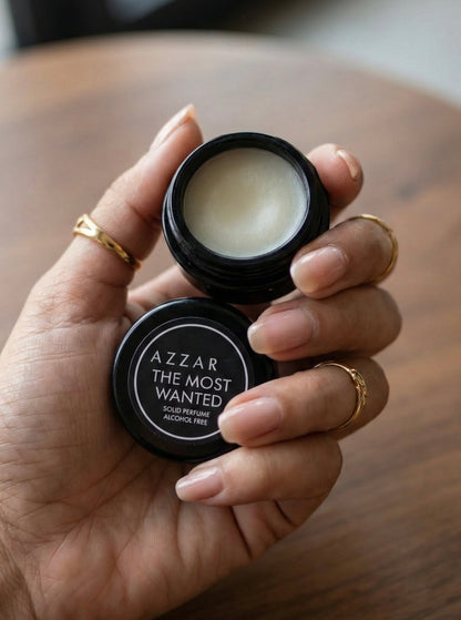 Hand holding a small black container of Azzaro The Most Wanted cologne.